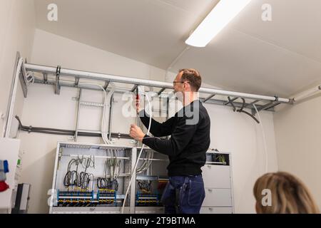 Männlicher Techniker, der Kabeldrähte an der Leiter im Messgeräteraum befestigt Stockfoto