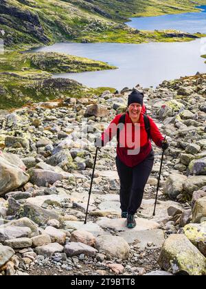 Lächelnde, reife Frau Skistöcke, die auf Felsen gegen den See laufen Stockfoto