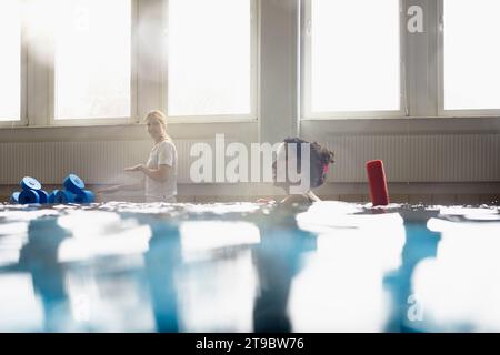 Lächelnde Frau mit Nudelschwaden im Schwimmbad im Rehabilitationszentrum Stockfoto