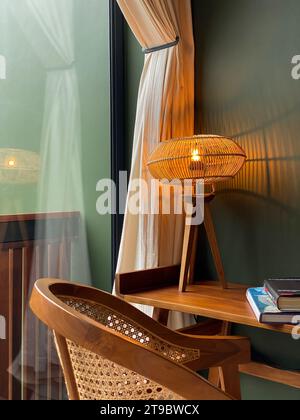 Tischleuchte mit Rattanschirm auf Holztisch mit Rattanstuhl Nahaufnahme Stockfoto