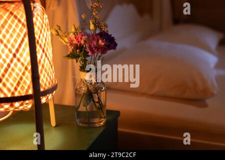 Auf dem Nachttisch im Schlafzimmer befindet sich eine Vase mit einem bescheidenen Blumenstrauß, die Atmosphäre und Komfort schafft Stockfoto