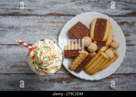 Schokoladen-Milchshake mit Schlagsahne, dekoriert mit Streuseln auf einem Holztisch. Milchshake und süße Kekse. Stockfoto