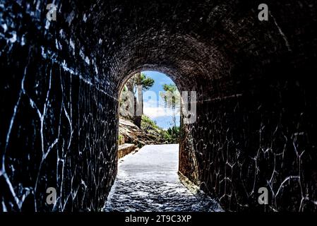 Blick aus dem Inneren eines Tunnels auf eine grüne Landschaft mit Bäumen und blauem Himmel. Zugang zum Strand Stockfoto