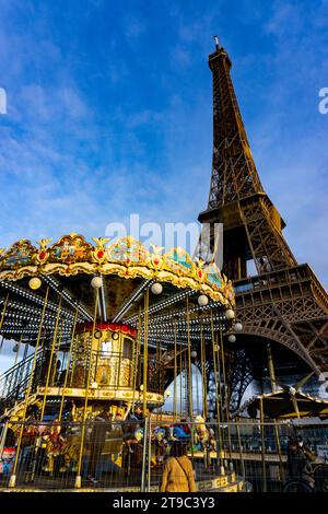 Ein goldenes Karussell dreht sich vor dem Hintergrund des Eiffelturms und des blauen Himmels und schafft eine skurrile Szene im Herzen von Paris. Romantisches Paris. Stockfoto