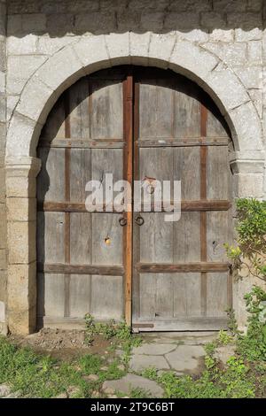 070 Alte farblose, zweiflügelige Holztür mit Rundbogen an Steinmauer, Rruga Kristaq Tutulani Straße, Gorica Viertel. Berat-Albanien. Stockfoto