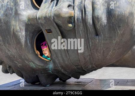 Krakau, Polen - 18. Juli 2023: Kleines Kind, das durch das Auge der riesigen Kopfstatue von Eros Bendato in der Region Rynek GlownyKrakau Malopolska in Polen blickt Stockfoto