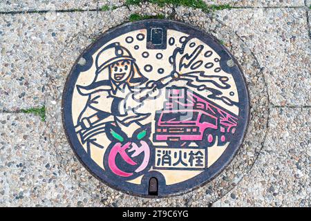 Japanische Manhole-Abdeckung in Fukuyama. Abbildung eines Tannenmotors und eines Feuerwehrmannes, der Wasser aus einem Schlauch sprüht, um die Feuerwehr zu feiern. Stockfoto