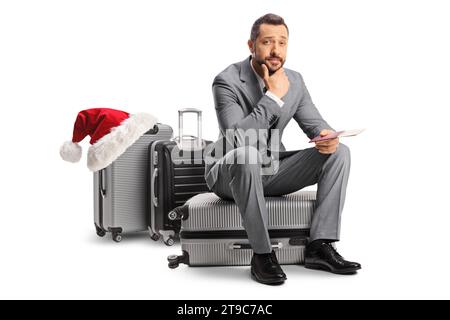 Nachdenklicher Geschäftsmann, der auf einem Koffer sitzt, verzögertes weihnachtsflugkonzept isoliert auf weißem Hintergrund Stockfoto
