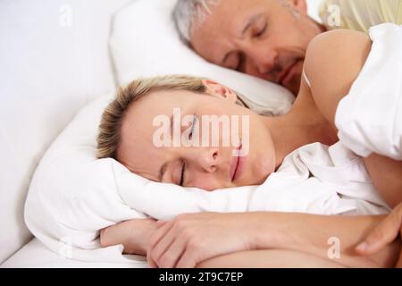 Liebe, müde und reife Paare schlafen im Bett, um am Wochenende zusammen zu kuscheln. Ruhiger, friedlicher und älterer Mann und Frau, die ein Nickerchen machen Stockfoto