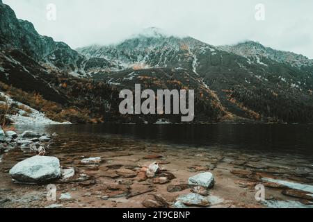 Wo das Flüstern des Flusses auf die standhafte Umarmung von Steinen trifft, eingerahmt von der majestätischen Silhouette entfernter Berge, die sich in einem leichten Nebel verstecken. Stockfoto