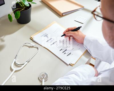 Anonymer männlicher Arzt in einem weißen Kleid, der medizinische Unterlagen in einer Klinik ausfüllt Stockfoto