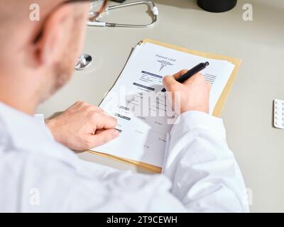 Anonymer männlicher Arzt in einem weißen Kleid, der medizinische Unterlagen in einer Klinik ausfüllt Stockfoto