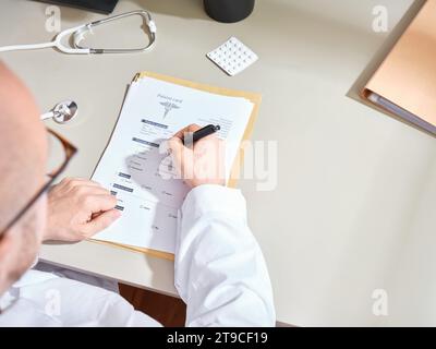 Anonymer männlicher Arzt in einem weißen Kleid, der medizinische Unterlagen in einer Klinik ausfüllt Stockfoto
