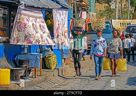 Madagassische Mädchen, die mit Waren auf dem Kopf auf der Straße laufen und Wasser in Kanistern in der Stadt Antananarivo, Analamanga, Madagaskar, Afrika transportieren Stockfoto