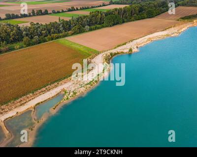 Felder und ein Wald neben dem Ufer eines künstlichen Sees mit türkisfarbenem Wasser im Herbst, von oben gesehen von einer Drohne Stockfoto