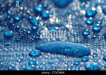 Große Tropfen und Spritzer Wasser liegen nach Regen auf einer blauen Plane Stockfoto