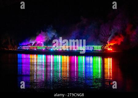 Kingswear, Devon, Großbritannien. November 2023. Der Christmas Train of Lights auf der Dartmouth Steam Railway in Devon, der zwischen dem 24. November und dem 30. Dezember 2023 verkehrt, spiegelt sich im ruhigen Wasser des Flusses Dart wieder, als er nach Paignton in Devon fährt, nachdem er Kingswear in Devon auf seiner Reise nach Paignton verlassen hat. Die Wagen und Dampflokomotiven des Festdienstes sind innen und außen mit farbigen Lichtern beleuchtet. Bildnachweis: Graham Hunt/Alamy Live News Stockfoto