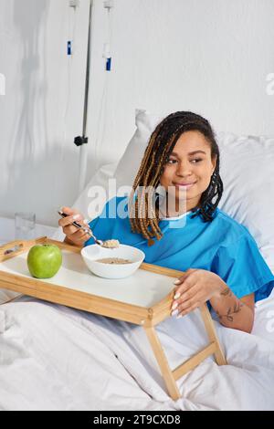 afroamerikanische Frau, die Haferbrei und Apfel zum Frühstück in ihrer Krankenhausstation, Gesundheitswesen Stockfoto