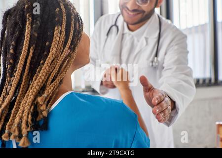 Zugeschnittene Ansicht eines fröhlichen indischen Arztes, der mit seinem fröhlichen afroamerikanischen Patienten die Hand schüttelt Stockfoto