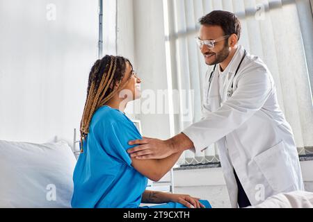 Fröhlicher indischer Arzt in Brille, der mit seinem fröhlichen afroamerikanischen Patienten die Hände schüttelt, Gesundheitswesen Stockfoto