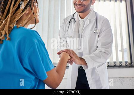 Zugeschnittene Ansicht eines fröhlichen indischen Arztes, der mit seinem fröhlichen afroamerikanischen Patienten die Hand schüttelt Stockfoto