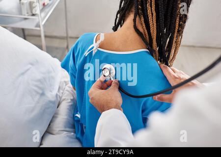 Rückansicht eines indischen Arztes, der den Atem seines afroamerikanischen Patienten auf der Krankenhausstation überprüft Stockfoto