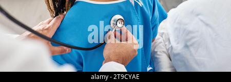 Rückansicht eines indischen Arztes, der den Atem seines afroamerikanischen Patienten auf der Krankenhausstation überprüft, Banner Stockfoto