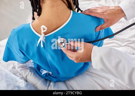 Rückansicht eines indischen Arztes, der den Atem seines afroamerikanischen Patienten auf der Krankenhausstation überprüft Stockfoto