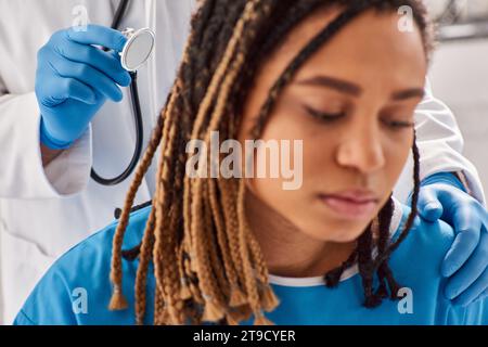 Fokus auf Arzt, der den Atem seines verschwommenen afroamerikanischen Patienten in der Krankenhausstation, Gesundheitswesen überprüft Stockfoto