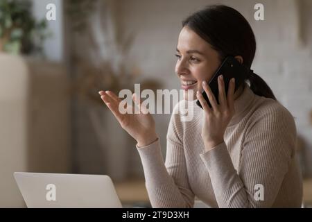 Hübsche Frau, die zu Hause eine angenehme Unterhaltung auf dem Handy hat Stockfoto