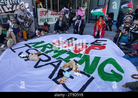 London, Großbritannien. November 2023. Eltern, Babys und Kinder umgeben einen Fallschirm, der mit der Aufschrift "BAE Stop Ararming Israel" bemalt ist, während eines Protestes der Eltern für Palästina innerhalb und außerhalb eines Gebäudes, in dem sich die Büros des Rüstungsunternehmens BAE Systems befinden, um einen Waffenstillstand in Gaza zu fordern und die britische Regierung den Waffenverkauf einzustellen nach Israel. Eltern protestierten in Solidarität mit palästinensischen Familien in Gaza, wo seit dem 7. Oktober 2023 nach Angaben des palästinensischen Gesundheitsministeriums über 5.800 Kinder bei israelischen Luftangriffen getötet wurden. Quelle: Mark Kerrison/Alamy Live News Stockfoto