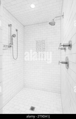 Eine große begehbare Dusche mit U-Bahn-Fliesen an den Wänden und am Boden, verchromte Duschköpfe und Wasserhahn und ein kleiner quadratischer Fliesenakzent. Stockfoto
