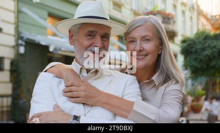 Porträt glückliche kaukasische Familie älteres Ehepaar Ehefrau umarmt Kuschelumarmung Blick in die Kamera außerhalb der Stadtstraße. Senioren genießen es Stockfoto
