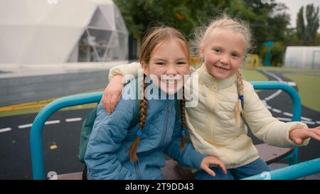 Zwei kleine Mädchen Freunde Schwestern reiten Schaukel Lachen Lächeln Freude Glück Kindheit Spielplatz Umarmung Spaß Schulmädchen spazieren spielen außerhalb der Stadt Kinder Stockfoto