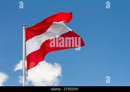 Die Flagge Österreichs winkt im Wind am Fahnenmast gegen den Himmel mit Wolken an sonnigem Tag, Nahaufnahme Stockfoto