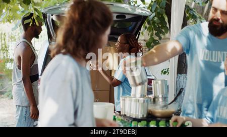 Das humanitäre Hilfsteam unterstützt arme Obdachlose mit Lächeln und Zusammenarbeit. afroamerikanische Freiwillige im Auto spenden Spendenboxen an Unterprivilegierte. Stativaufnahme. Stockfoto