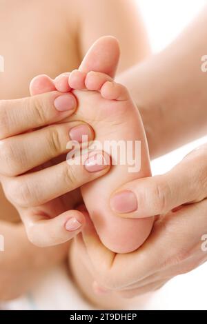 Nahaufnahme einer Mutter, die sanft die Füße und Fußsohlen ihres kleinen Kindes auf weißem Hintergrund massiert. Stockfoto