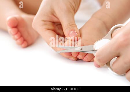 Nahaufnahme einer Mutter, die sanft den Fuß ihres kleinen Kindes hält und Zehennägel auf weißem Hintergrund schneidet. Stockfoto