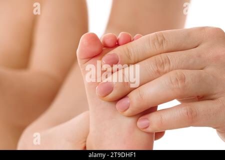 Nahaufnahme einer Mutter, die sanft die Füße und Fußsohlen ihres kleinen Kindes auf weißem Hintergrund massiert. Stockfoto