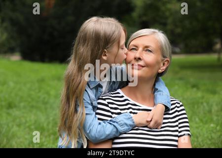 Glückliche Enkelin küsst ihre Großmutter im Park, Platz für SMS Stockfoto