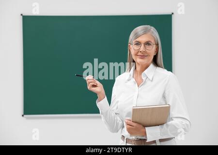 Porträt des Professors mit Stift und Notizbuch in der Nähe der Tafel im Klassenzimmer, Raum für Text Stockfoto