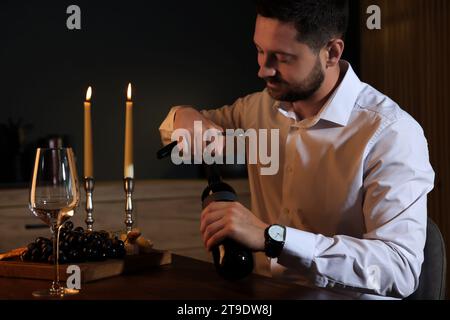 Romantisches Abendessen. Mann öffnet eine Weinflasche mit Korkenzieher am Tisch drinnen Stockfoto