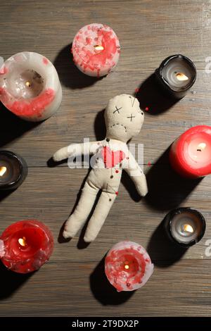 Voodoo-Puppe mit Nadeln im Kreis brennender Kerzen auf Holztisch, flach gelegt Stockfoto