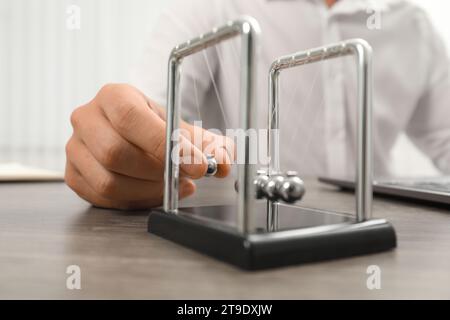 Mann, der mit Newtons Wiege am Tisch spielt, Nahaufnahme. Physikalisches Gesetz der Energieeinsparung Stockfoto