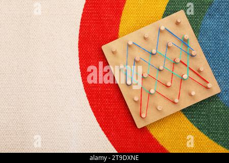 Motorische Entwicklung. Geoboard aus Holz mit Gummibändern auf Teppich, Blick von oben. Leerzeichen für Text Stockfoto