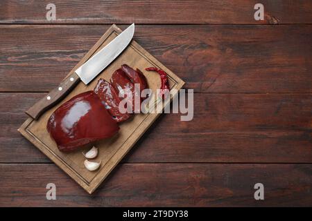 Schneiden Sie rohe Rinderleber mit Chili, Knoblauch und Messer auf einem Holztisch, von oben. Leerzeichen für Text Stockfoto