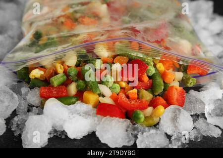 Reißverschlusstasche mit verschiedenen gefrorenen Gemüsesorten und Eis auf dem Tisch, Nahaufnahme Stockfoto