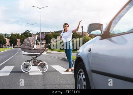 Eine empörte Mutter mit dem Kinderwagen, der mit einem Autofahrer auf dem Straßenübergang in Konflikt steht. Konzepte der Sicherheit und Verkehrsordnung. Stockfoto