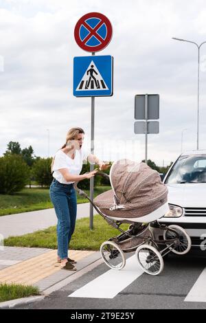 Schockierte Mutter auf dem Gehweg nach einem Autounfall, als ein Fahrzeug ihren Kinderwagen trifft. Konzepte von Sicherheit, Verkehrsordnung und Versicherung. Stockfoto