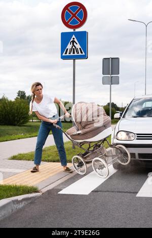 Mutter auf dem Fußweg nach einem Autounfall, als das Fahrzeug ihren Kinderwagen trifft. Konzepte von Sicherheit, Verkehrsordnung und Versicherung. Stockfoto